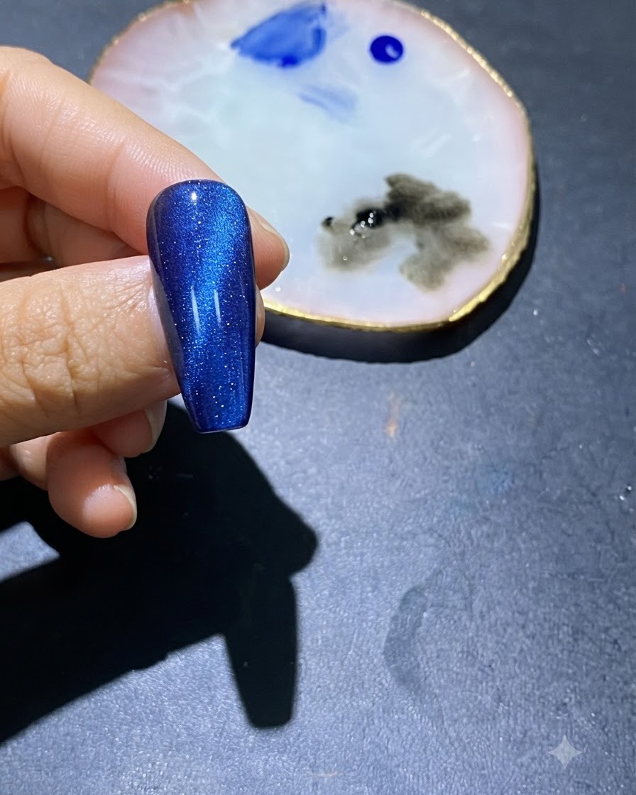 Gros plan dun ongle en gel œil-de-chat bleu avec des touches de vernis bleu au centre et une palette de nail art à proximité.