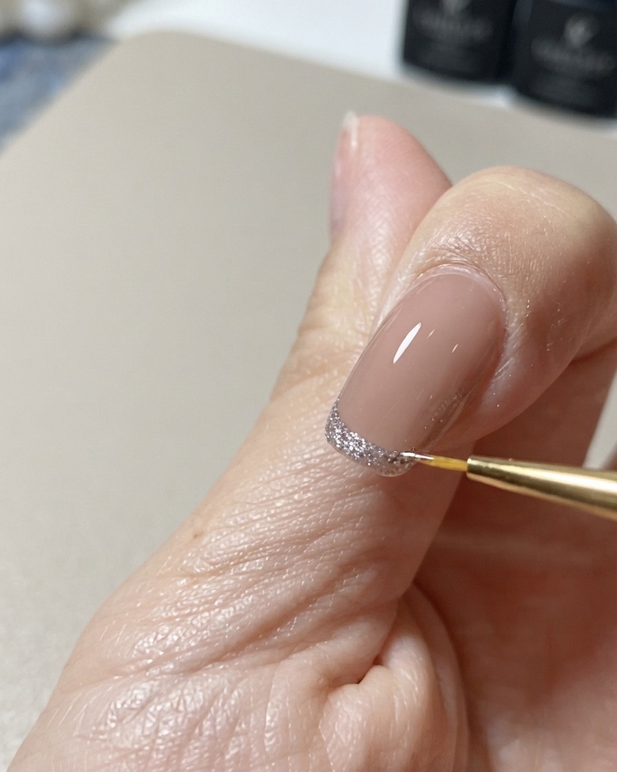 Un pinceau fin pour nail art nettoyant et parachevant le bord dun design de pointe œil-de-chat pailleté.