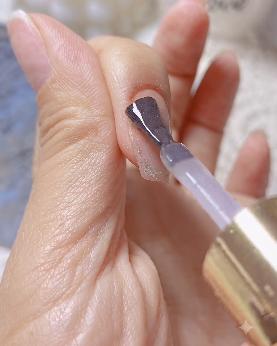 Un pinceau appliquant un gel de construction ou de renforcement transparent sur un ongle scintillant effet œil-de-chat.