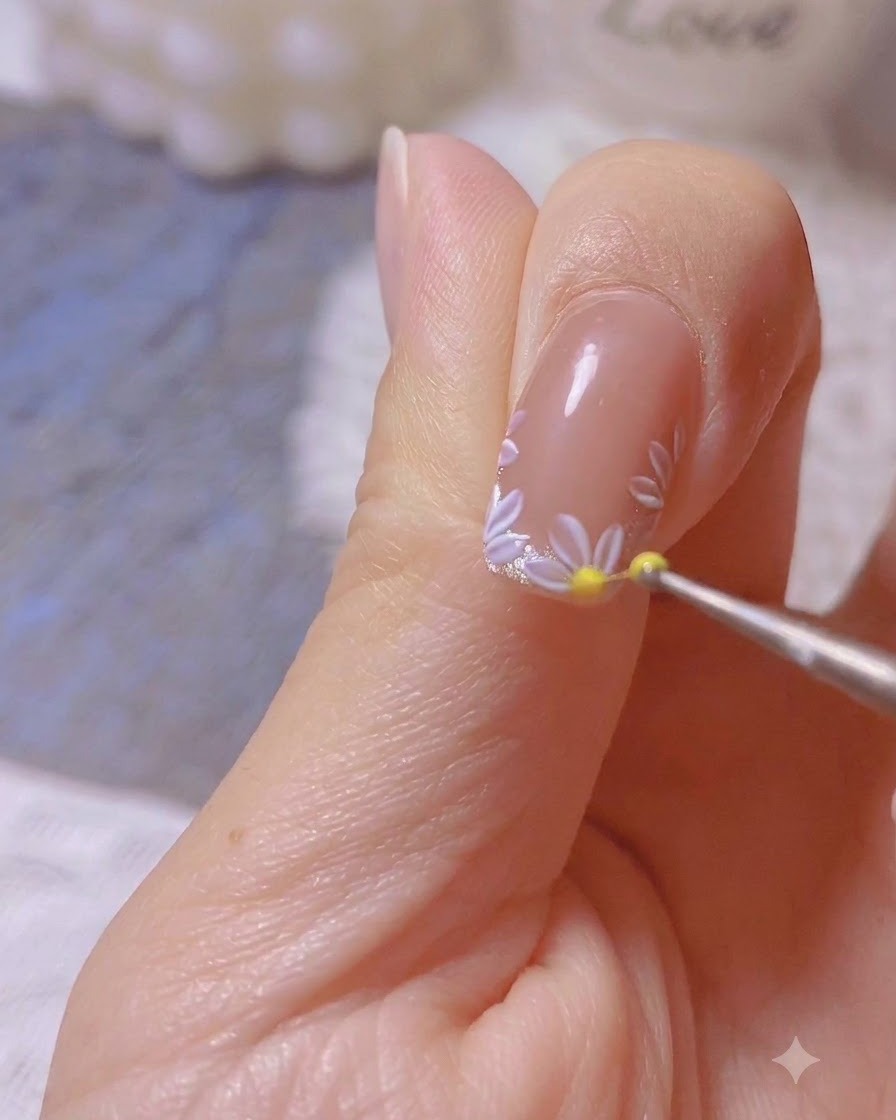 Un outil de dotting plaqué déposant un point jaune au centre dun design de marguerite blanche peint en nail art.