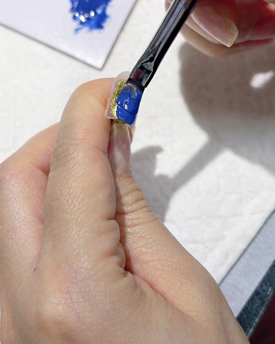 Un pinceau appliquant soigneusement un vernis gel bleu foncé riche sur un ongle artificiel.
