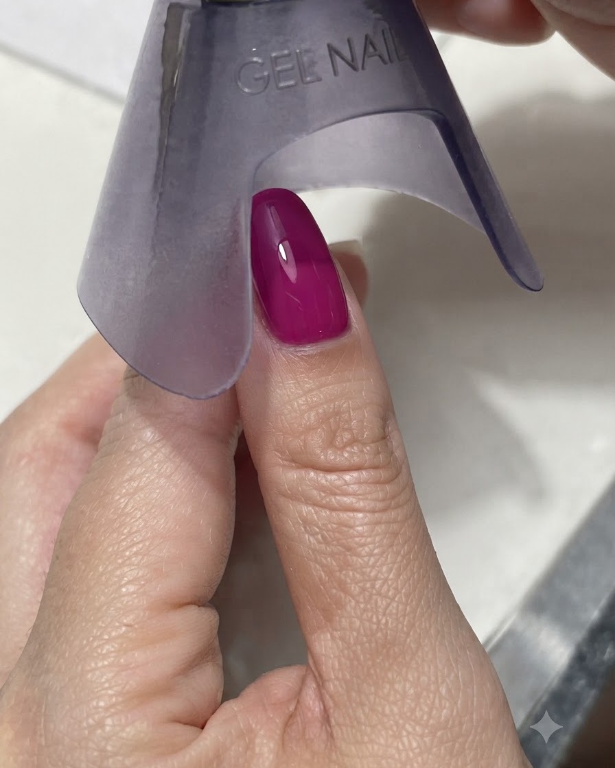 Une lampe UV/LED portable violette catalysant un ongle magenta foncé ou bleu vibrant sous une lumière vive.