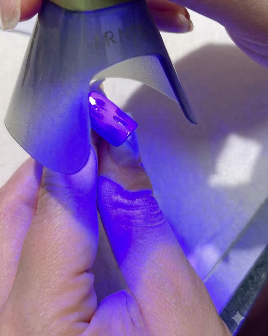 Une lampe UV violette portable catalysant un nail art de feuilles vert foncé sur un ongle peint en bleu.
