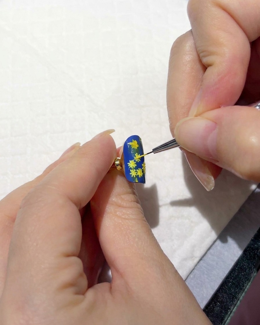 Une main tenant un ongle sous une lampe de polymérisation portable.