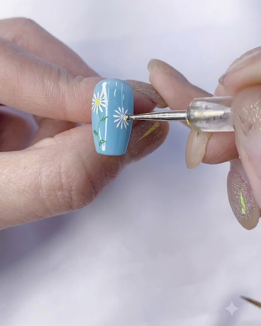 Un outil de dotting appliquant un point de centre jaune sur une marguerite blanche sur un ongle bleu.