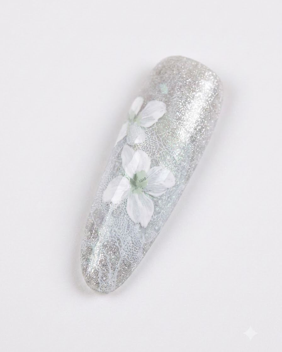 Gros plan dun ongle manucuré présentant de délicates fleurs blanches avec un léger ombrage gris sur un fond gris-bleu scintillant.
