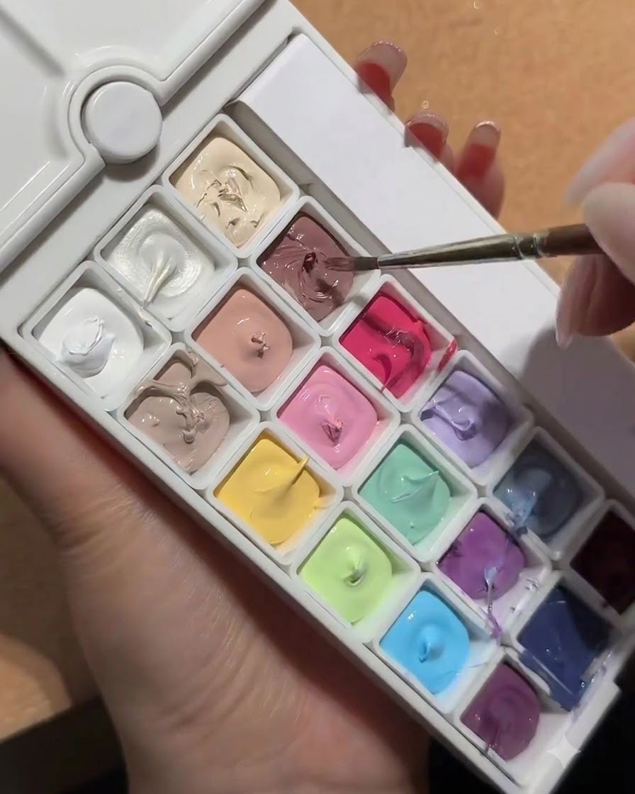 Un pinceau à nail art plongeant dans une palette contenant un carré de gel blanc pêche nud.