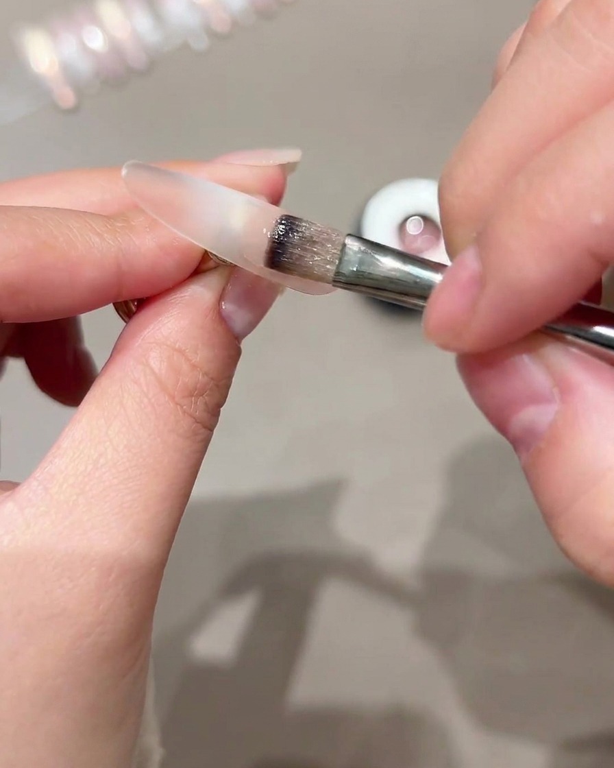 Un pinceau appliquant du gel cat-eye sur la partie extérieure dune capsule dongle transparente.