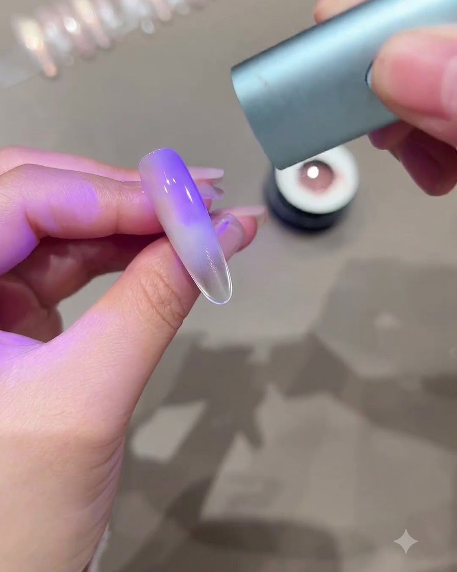 Une main tenant une mini lampe de polymérisation UV LED au-dessus dun ongle allongé montrant un effet cat-eye dégradé violet.