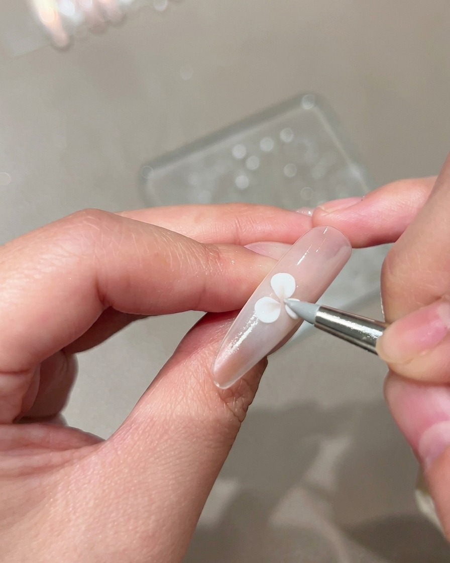 Un pinceau de modelage en silicone pressant et façonnant un pétale en gel blanc sur un ongle nude manucuré.
