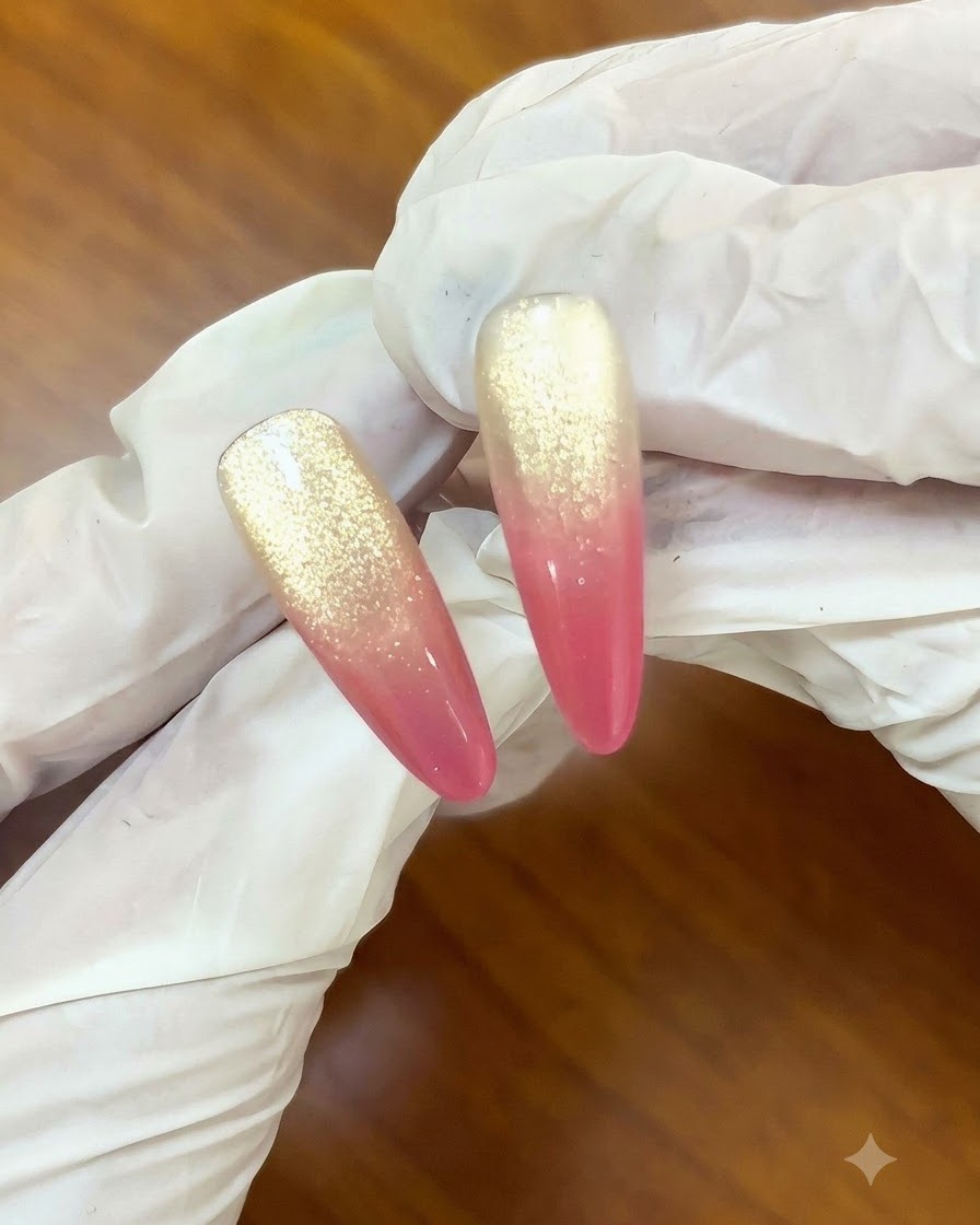 Un pinceau appliquant une couche de finition transparente sur un design dongles dégradé cat-eye rose coucher de soleil et doré.