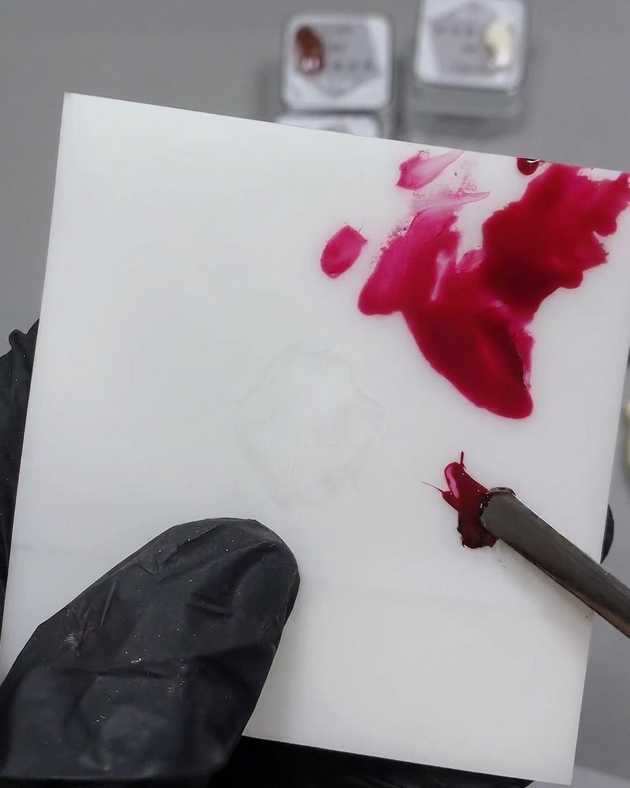 Un outil métallique mélangeant du gel noir dans une noisette de gel rouge sur une palette blanche.