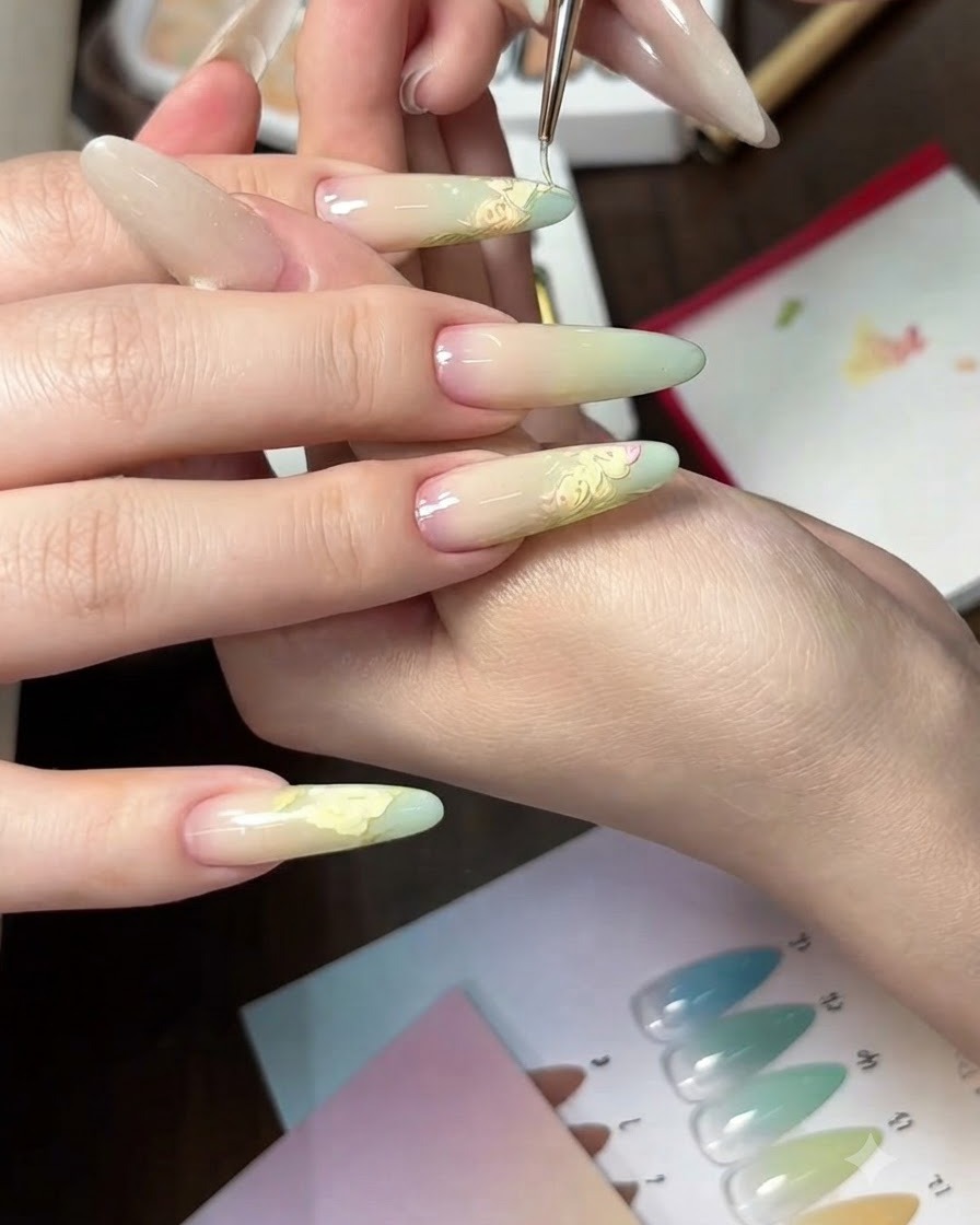 Vue rapprochée de lapplication dun dégradé de gel vert clair sur les pointes dongles de forme ovale à laide dune éponge.