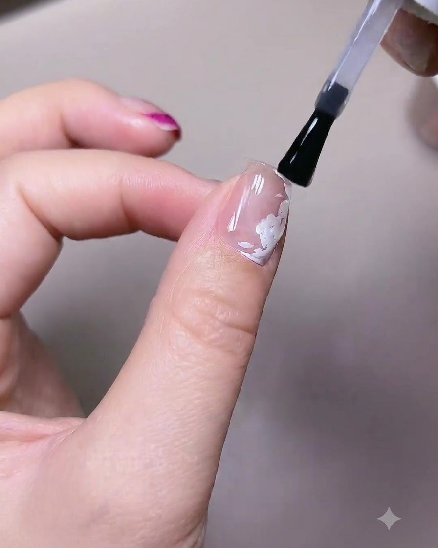 Un pinceau appliquant une couche de gel de finition mat sur un ongle comportant des éléments de roses blanches pré-peints.