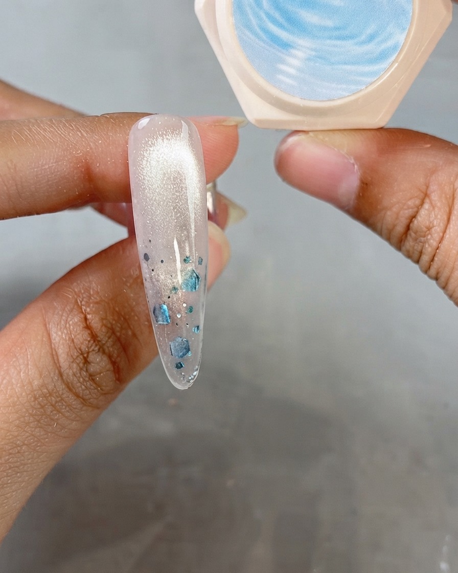 Un ongle en amande montrant une finition cat-eye chatoyante avec un pot de gel crystal en arrière-plan.