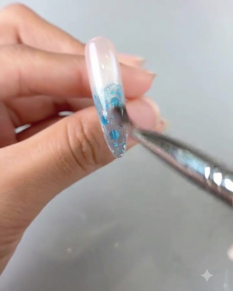 Vue rapprochée dun pinceau mélangeant du gel bleu sur un ongle pour créer un dégradé ombré.