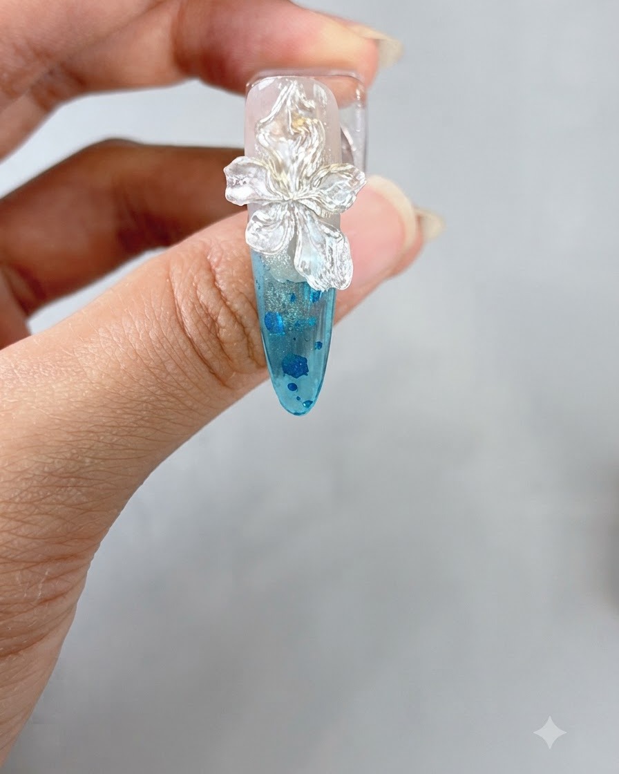 Une paire de brucelles plaçant une petite perle blanche au centre dune fleur 3D sculptée sur un ongle.