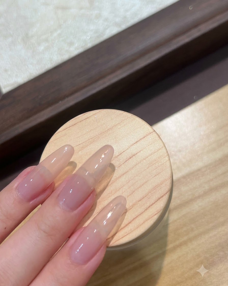 Gros plan sur de longs ongles en gel nude en cours de préparation avec une couche de gel de base transparent.
