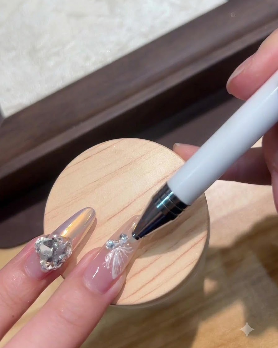 Un stylo à dotting plaquant un minuscule cristal à côté dun charm dongle papillon blanc.