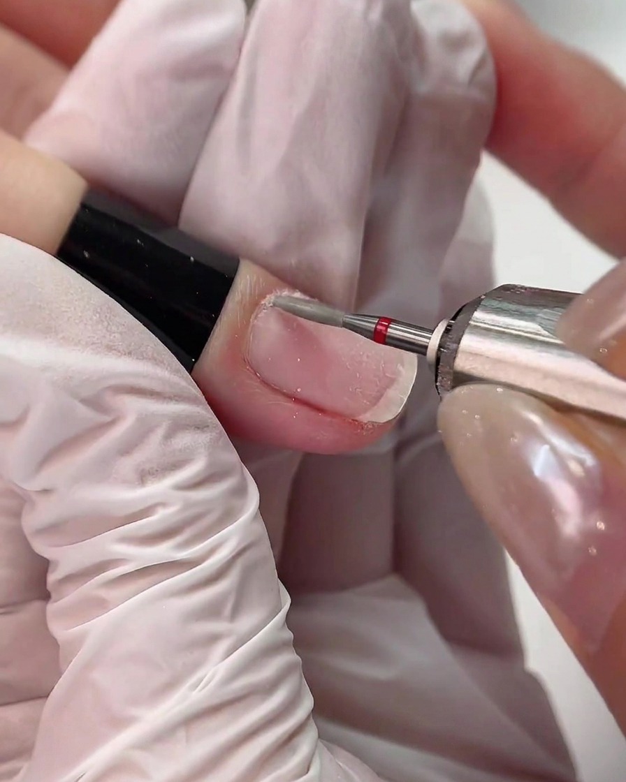 Une ponceuse électrique munie dun embout diamant à bague rouge travaillant délicatement le long de la ligne des cuticules dun doigt.