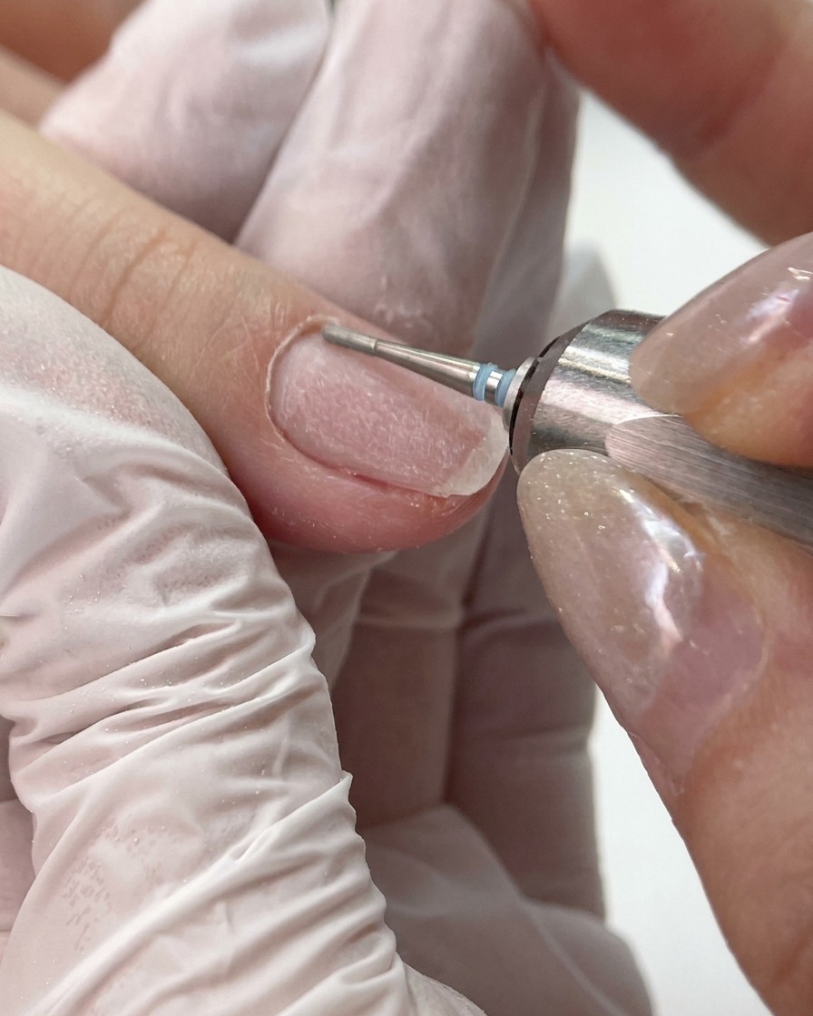Un petit embout de ponceuse à grain fin nettoyant et lissant le repli latéral et la zone des cuticules dun ongle.