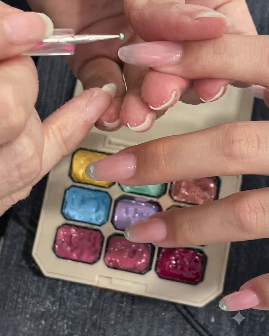 Outil de détail ou éponge tamponnant un pigment vert clair sur le bout dun ongle à côté dune palette de couleurs.