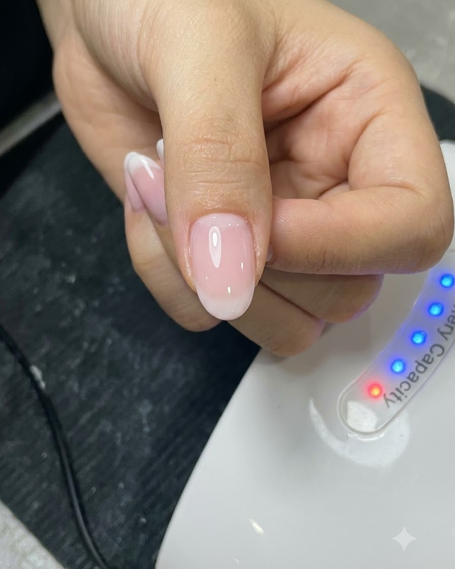 Pinceau appliquant une couche de top coat sur un ongle manucuré devant une lampe UV.