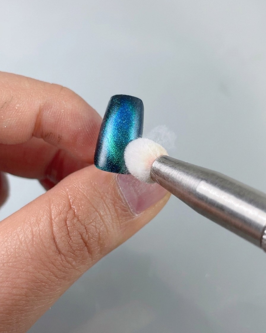 Un outil éponge tamponnant du gel stamping noir sur le bord dune pièce dongle cat-eye bleu-vert.
