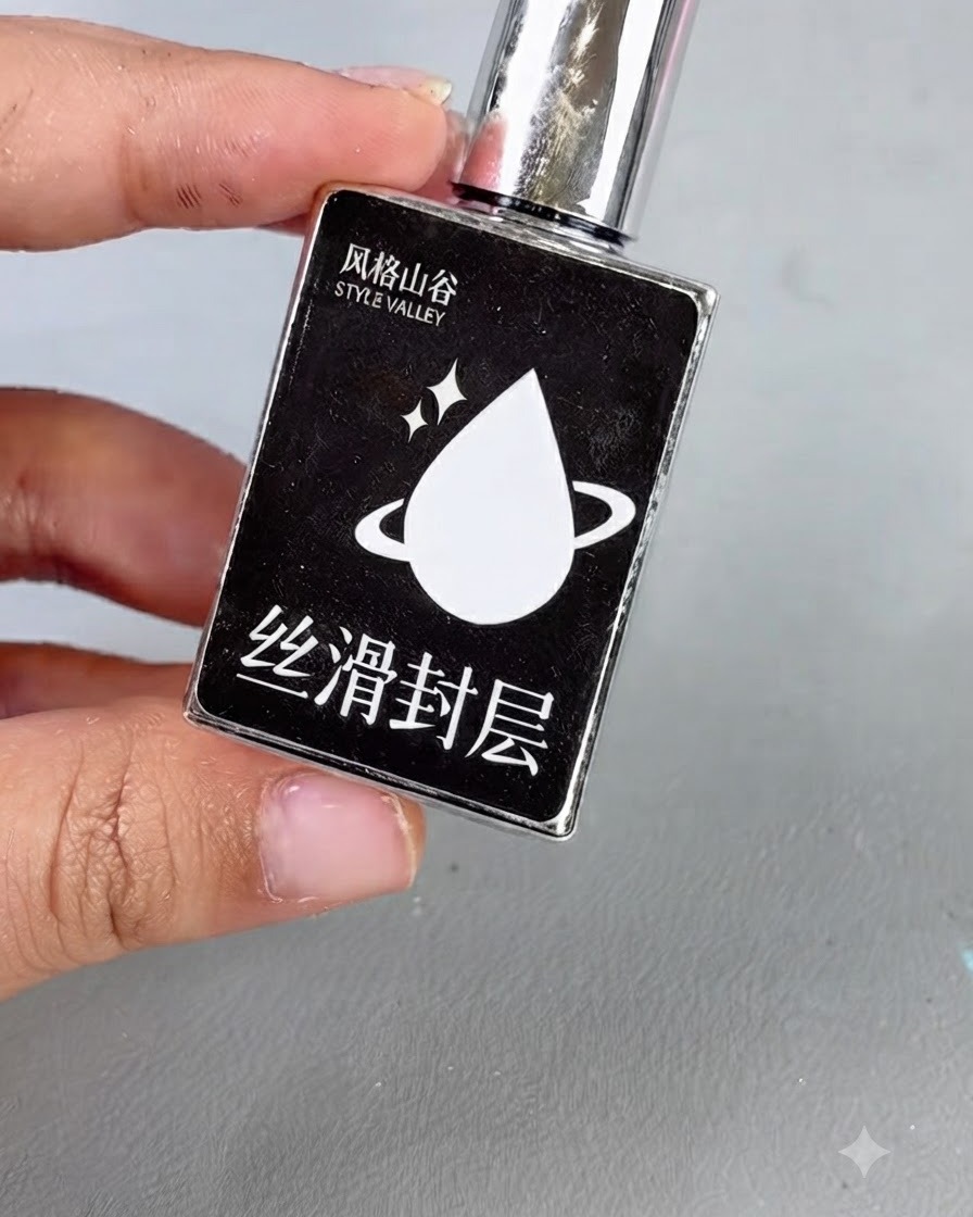 Une bouteille noire avec un bouchon argenté et une icône de goutte blanche étiquetée avec du texte, représentant un gel top coat lisse.