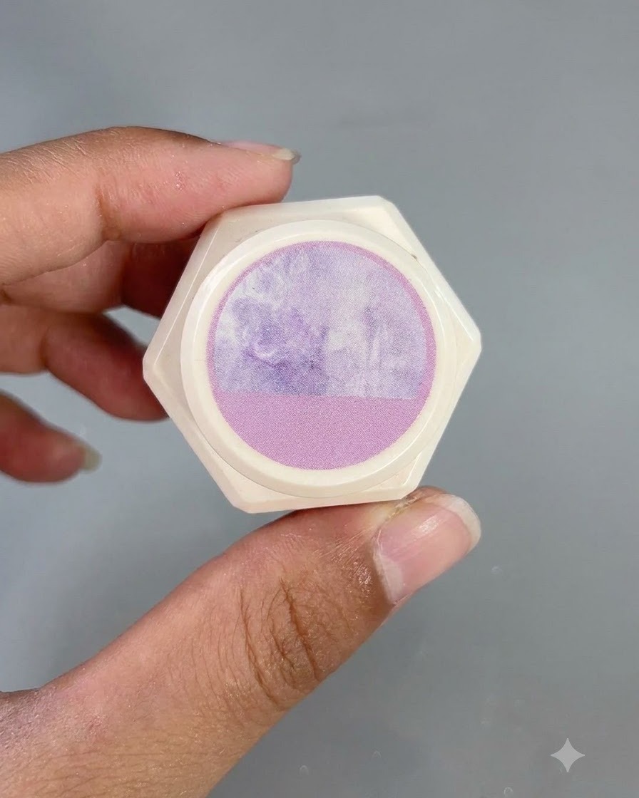 Un contenant hexagonal blanc avec un autocollant à motif aquarelle violet sur le couvercle, tenu par des doigts.