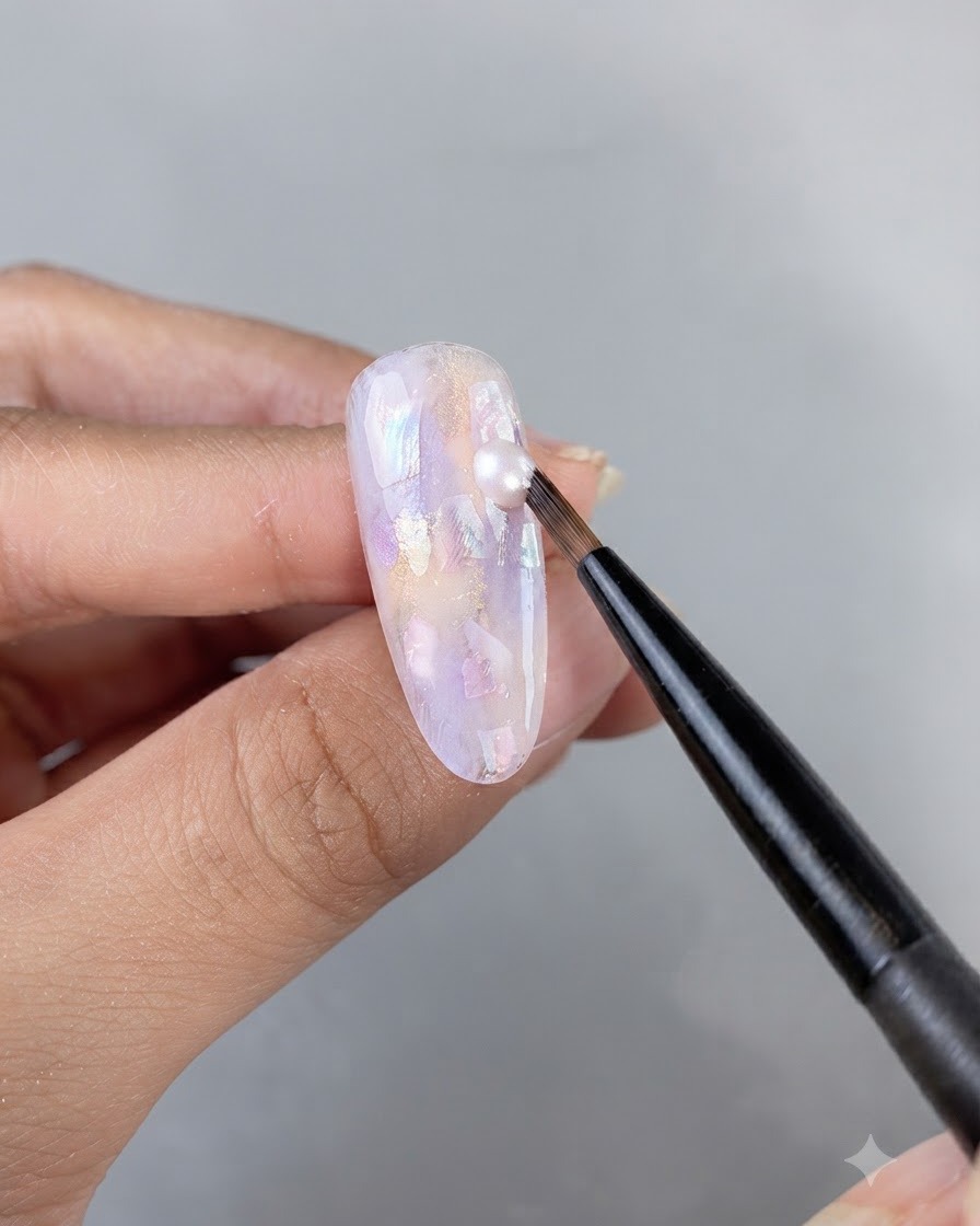 Un pinceau fin appliquant une goutte de gel scintillant sur une surface dongle ornée et incrustée de coquillages.