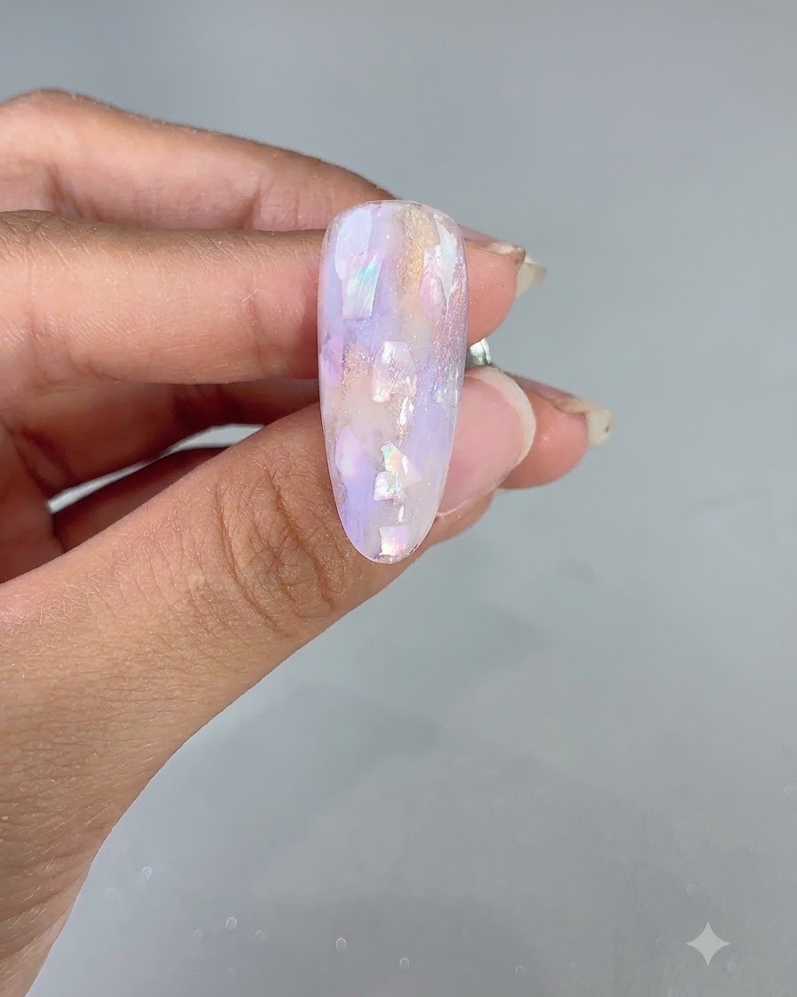 Gros plan dun ongle décoré de motifs violets et incrustés de coquillages après une catalyse flash.