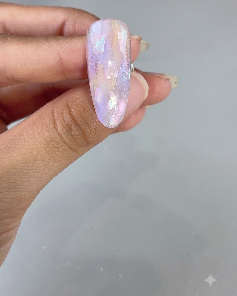 Un ongle fini en forme damande présentant un design brillant à laquarelle violette et coquillages.