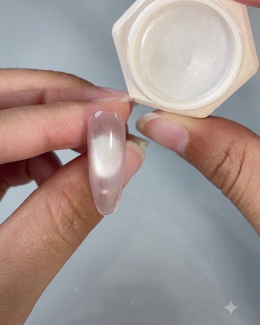 Un ongle en gel œil-de-chat fini présenté à côté de son pot de produit ouvert sous un éclairage de studio.