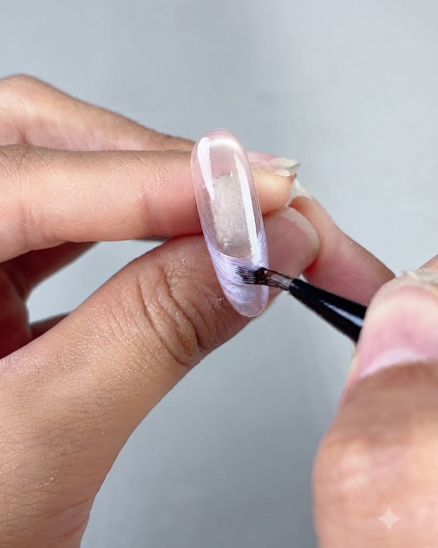 Un pinceau fin de nail art dessinant une ligne de French tip nacrée sur une extension dongle sculptée transparente.