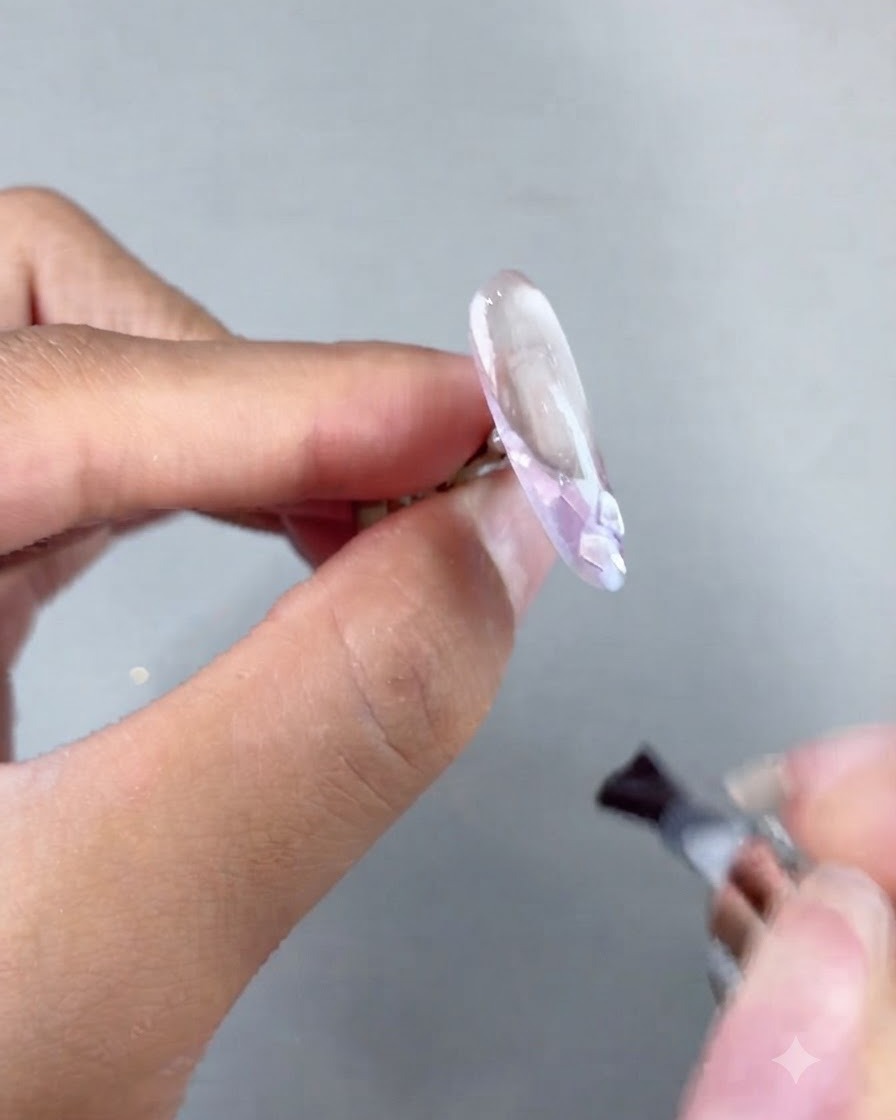Un pinceau appliquant du gel de construction souple sur une extension dongle décorée avant la catalyse.