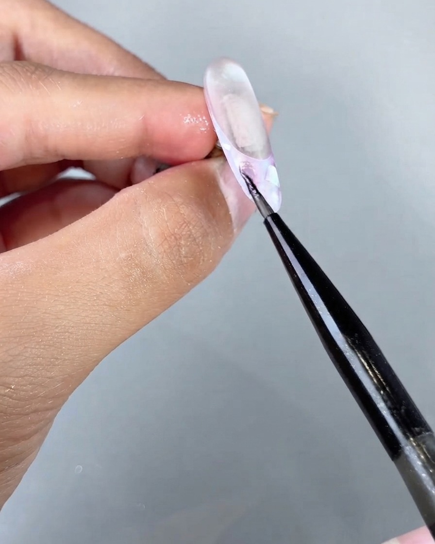 Un pinceau fin appliquant du gel œil-de-chat Magical Sea sur une section spécifique dun design dongle texturé.