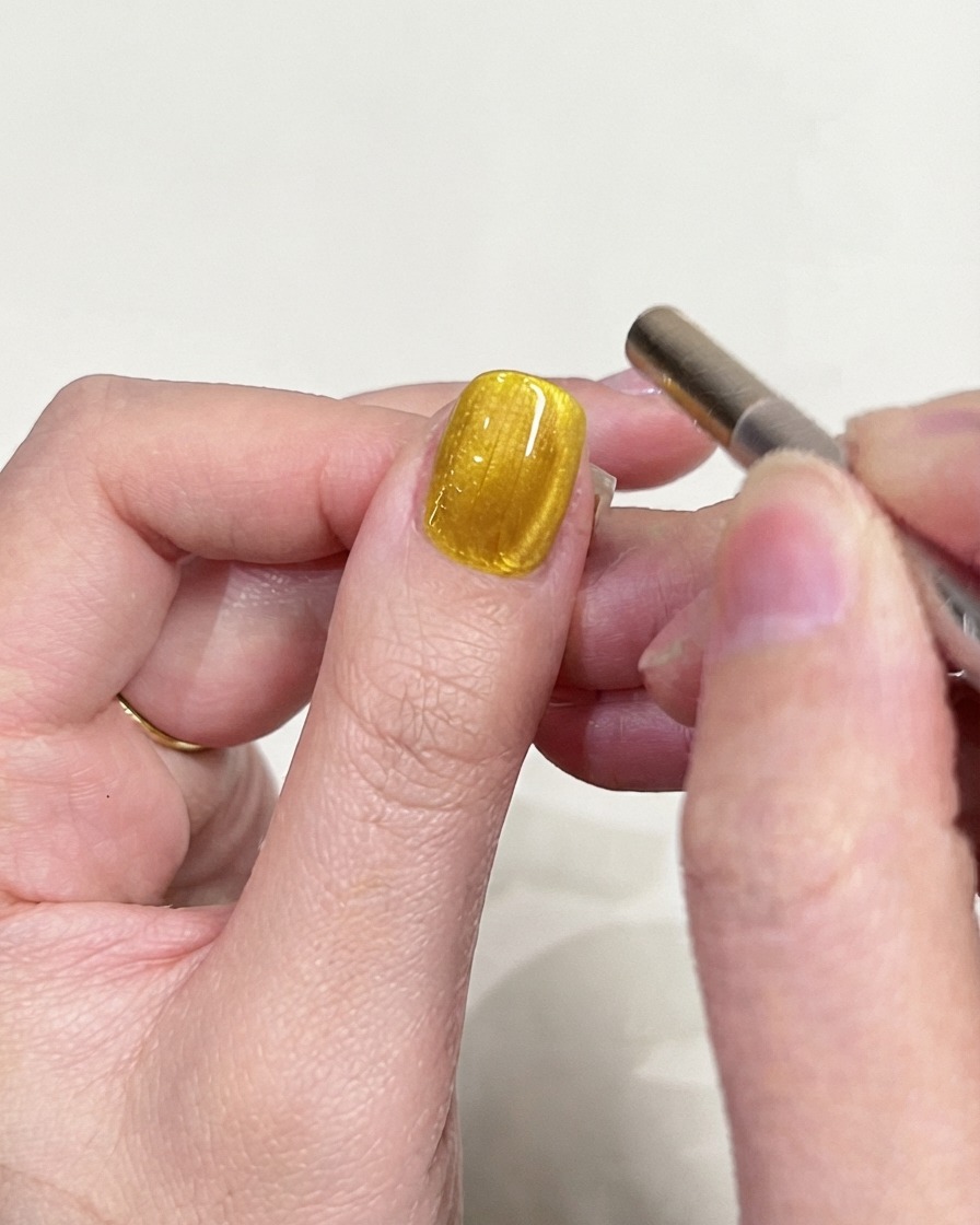 Photo dinspection détaillée dun ongle en gel œil-de-chat jaune se focalisant sur le reflet lumineux magnétique.