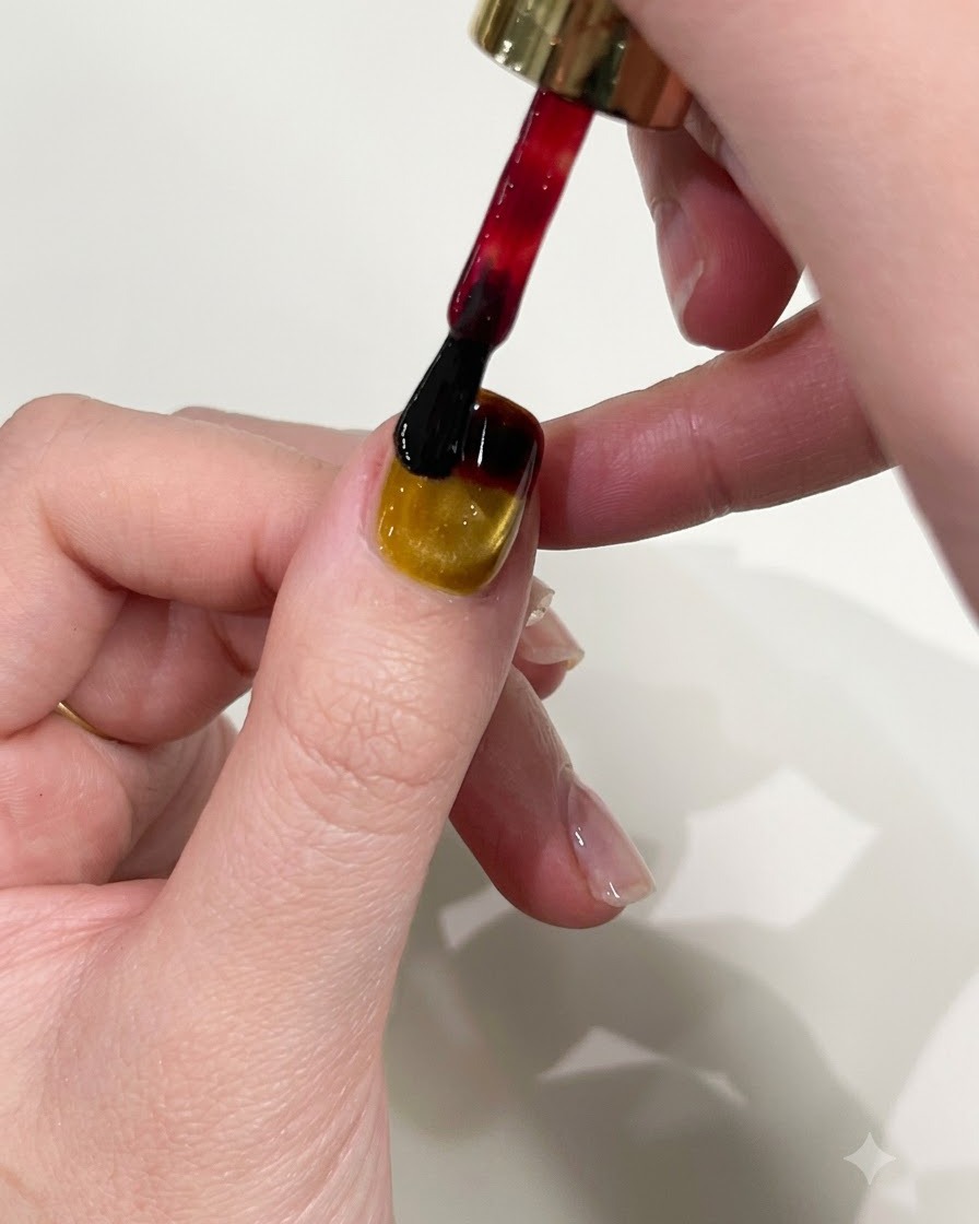 Un pinceau à vernis à ongles appliquant du gel rouge sur le bord supérieur dun ongle manucuré en jaune œil-de-chat.