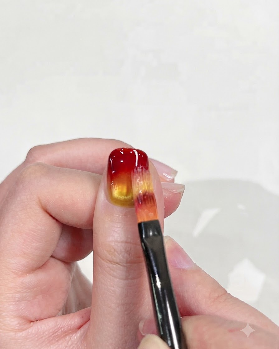 Un pinceau à ongles plat estompant soigneusement le bout rouge vers le bas dans la base jaune pour affiner leffet dégradé.