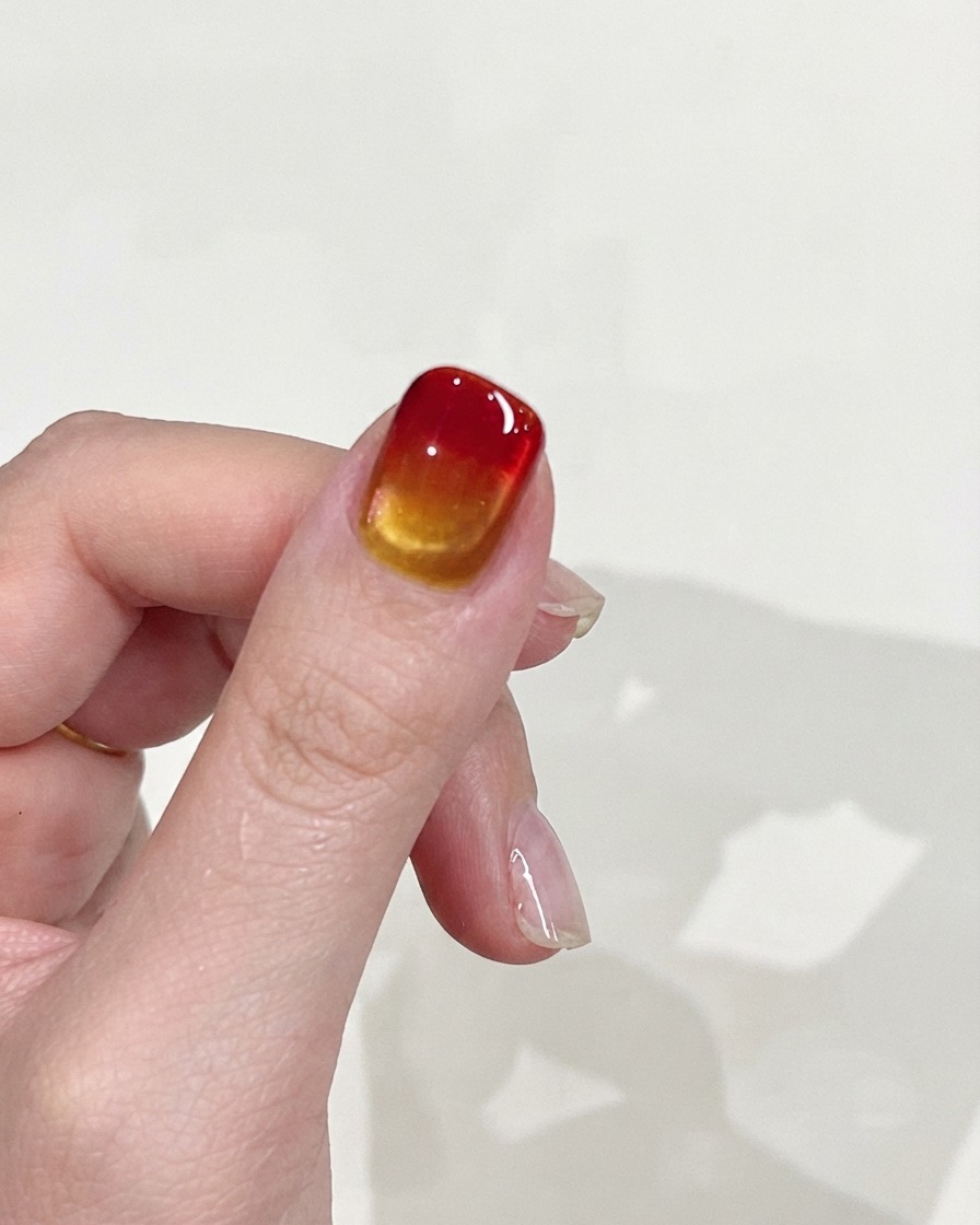 Une main levée contre un fond uni, affichant la texture dégradée lisse et la finition brillante de longle.