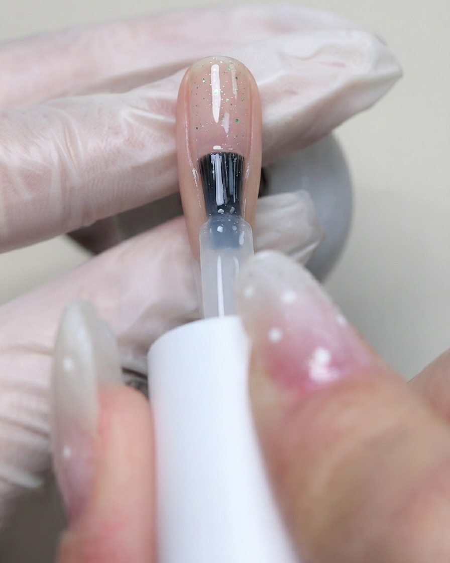 Un pinceau appliquant du gel de base flexible C7 transparent sur la surface de longle pour sceller les sequins disposés.