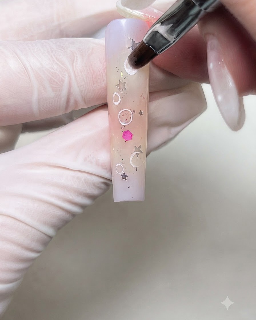 Un pinceau pour nail art adoucissant délicatement les contours intérieurs de cercles blancs en gel crème sur un ongle en dégradé.