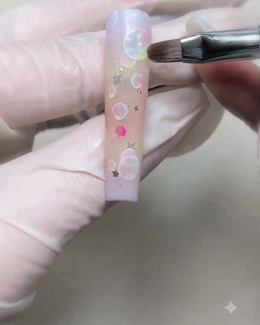 Une main gantée posant un sequin détoile argenté sur un ongle dégradé à laide dun pinceau fin.