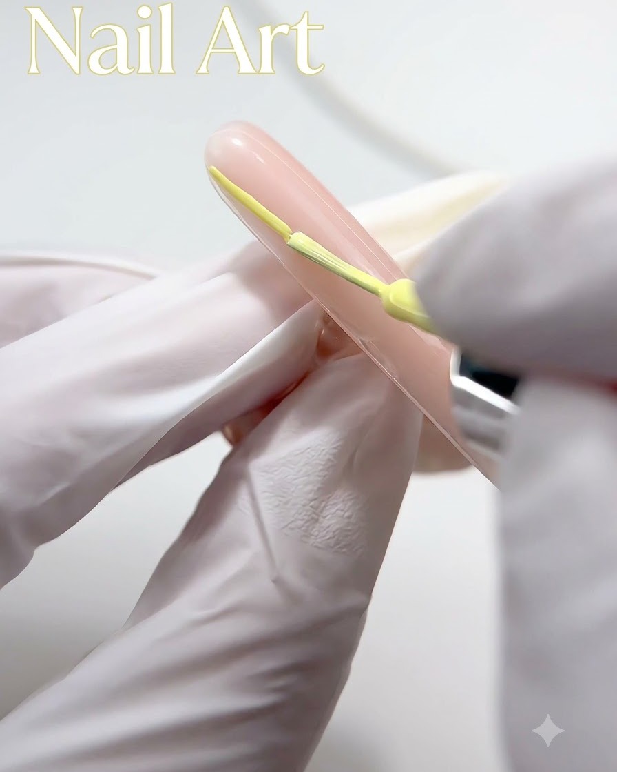 Une main gantée utilisant un pinceau fin pour appliquer du vernis gel jaune sur le bout dun ongle nude.