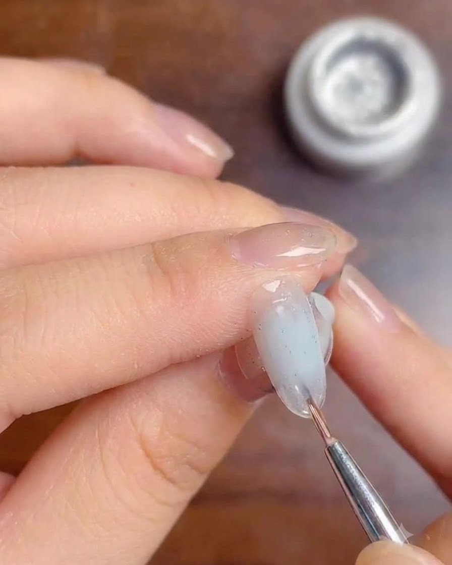 Un pinceau fin appliquant une couche de gel top coat transparent sur les lignes argentées dun ongle ombré.