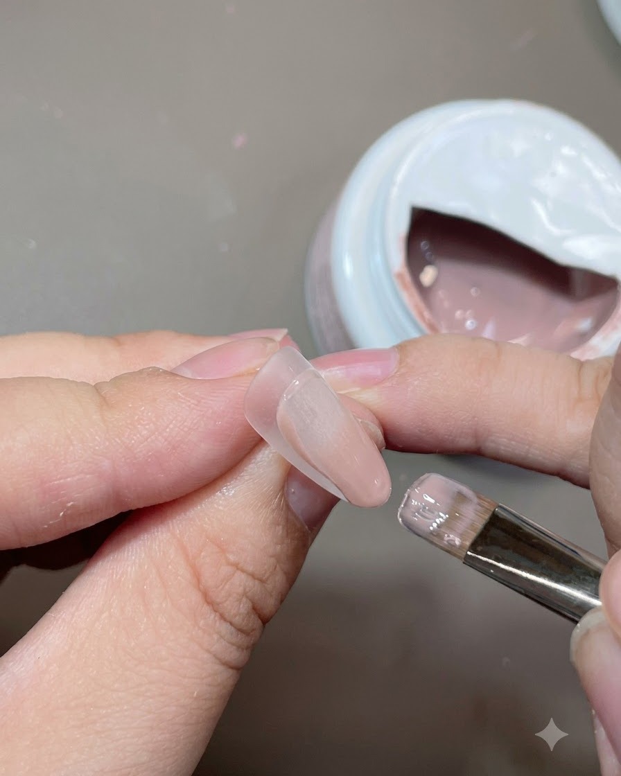 Un pinceau à gel plat appliquant une couleur de base nude sur une capsule dextension dongle.