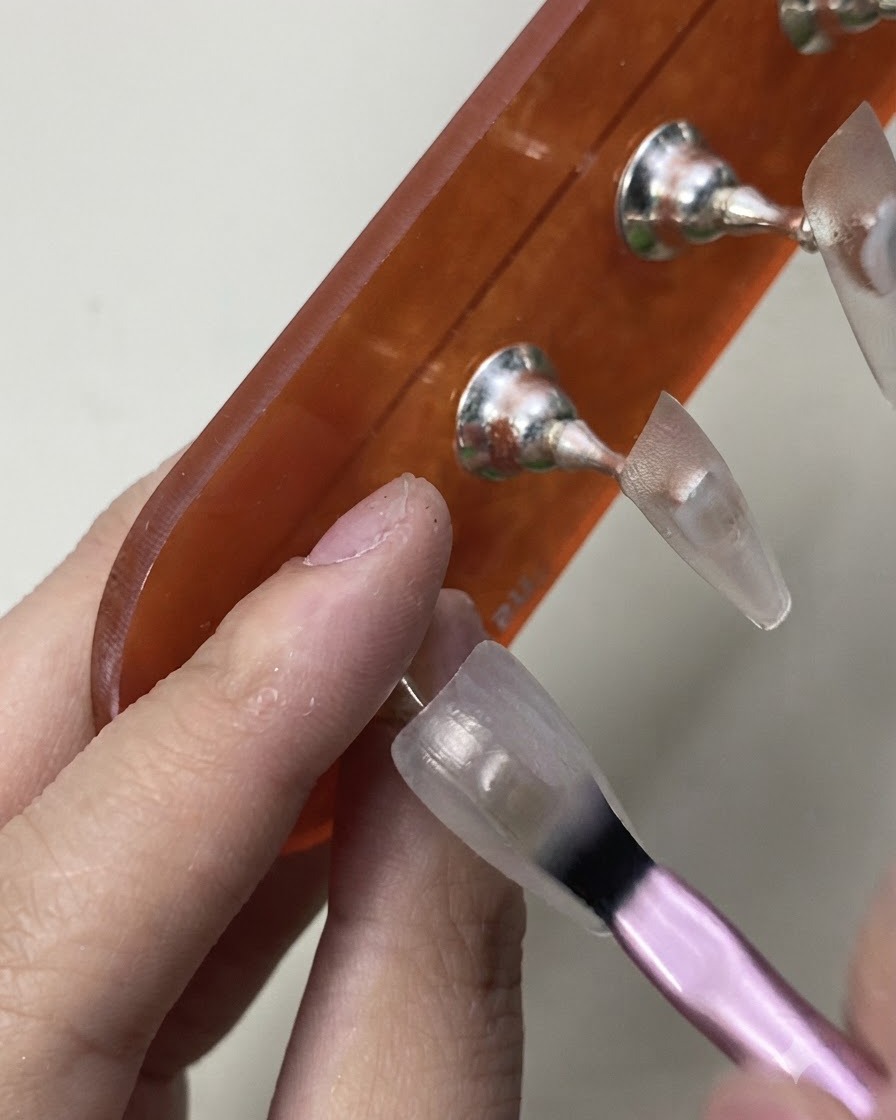 Un pinceau appliquant délicatement la première couche de vernis gel blanc laiteux translucide sur une capsule dongle dentraînement.