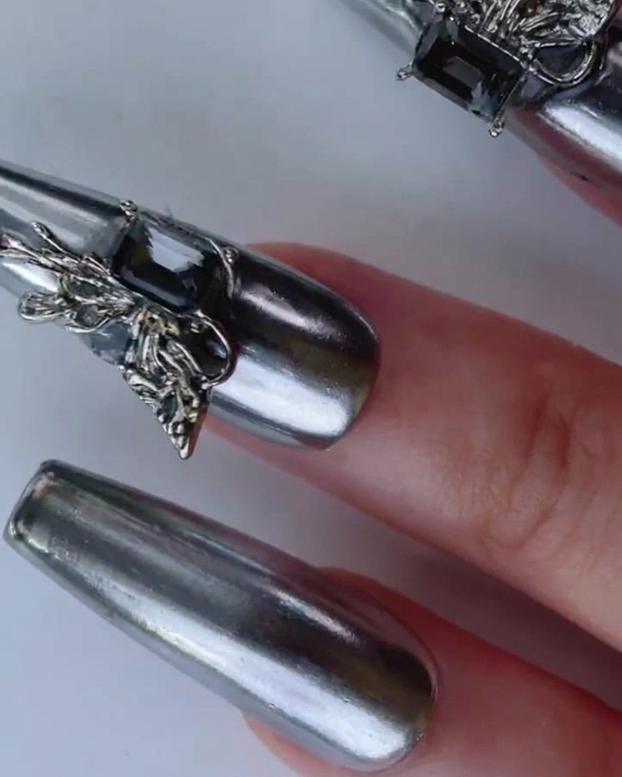 Une main inclinant un ongle chrome argenté sous un éclairage lumineux pour mettre en valeur sa finition miroir réfléchissante dynamique.