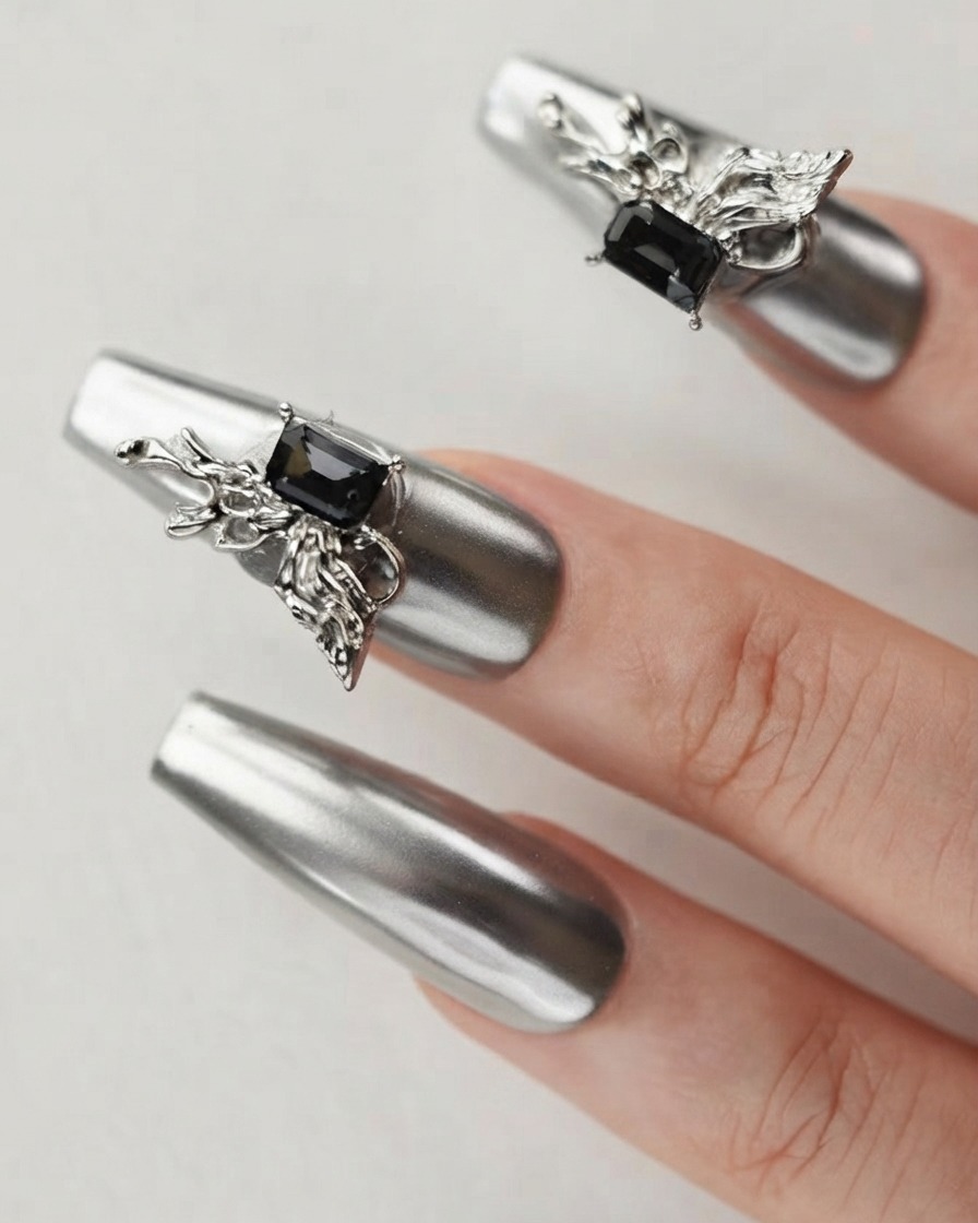 Gros plan dun doigt montrant un ongle chrome argenté orné dun charm papillon 3D détaillé et dun cristal sombre.